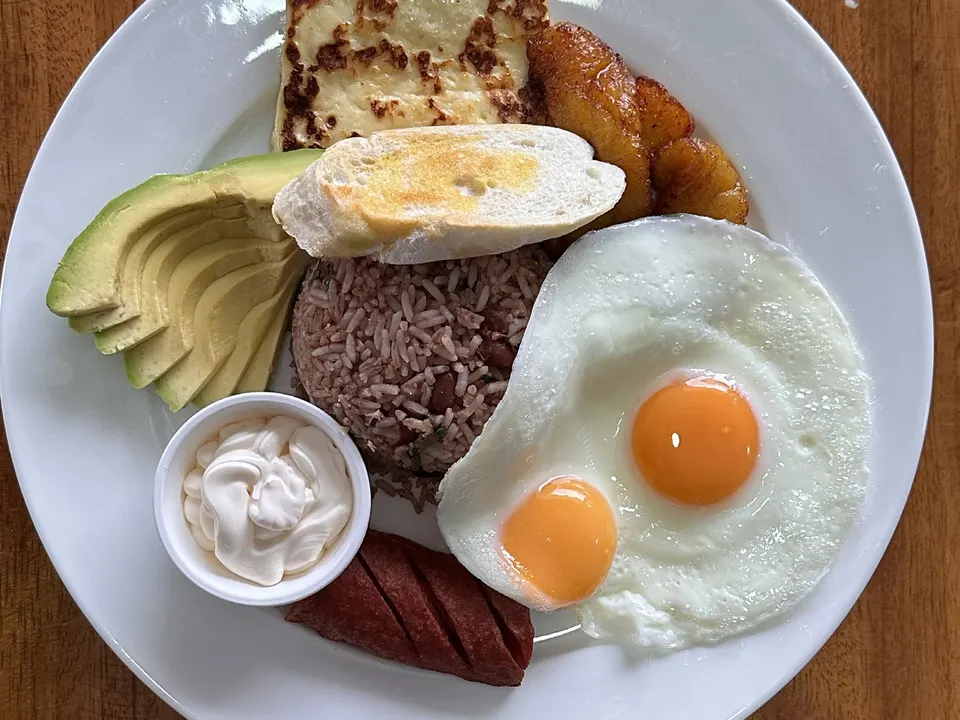 Desayuno típico con gallo pinto, dos huevos fritos, queso frito, plátano maduro, aguacate, natilla y salchichón