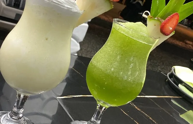 Dos cócteles tropicales, uno blanco y otro verde, decorados con piña