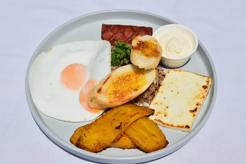 Desayuno con huevos fritos, gallo pinto, queso frito, salchichón, natilla, pan tostado y plátano maduro